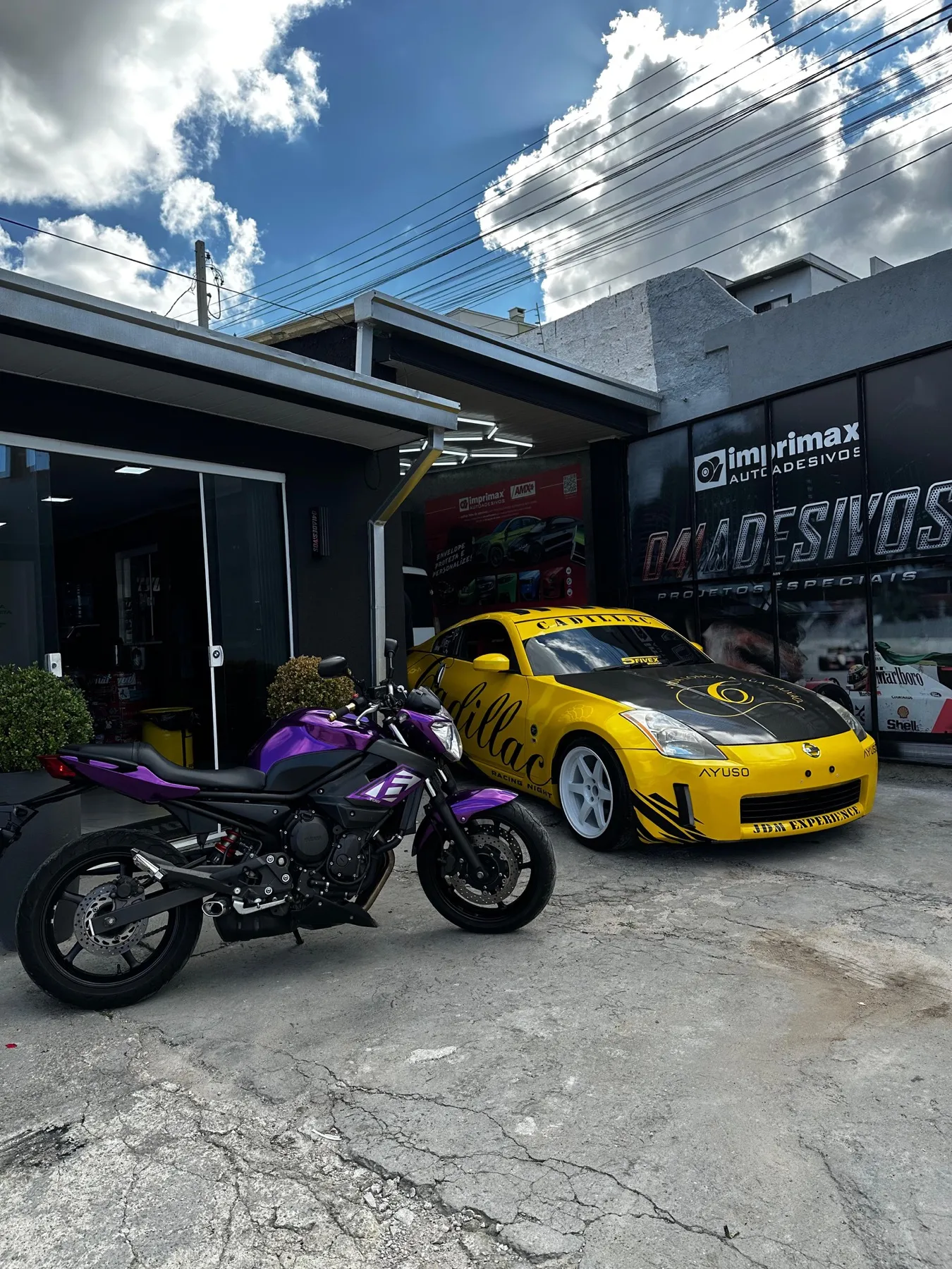 Nissan 350Z amarelo envelopado ao lado de moto Yamaha XJ6 roxa