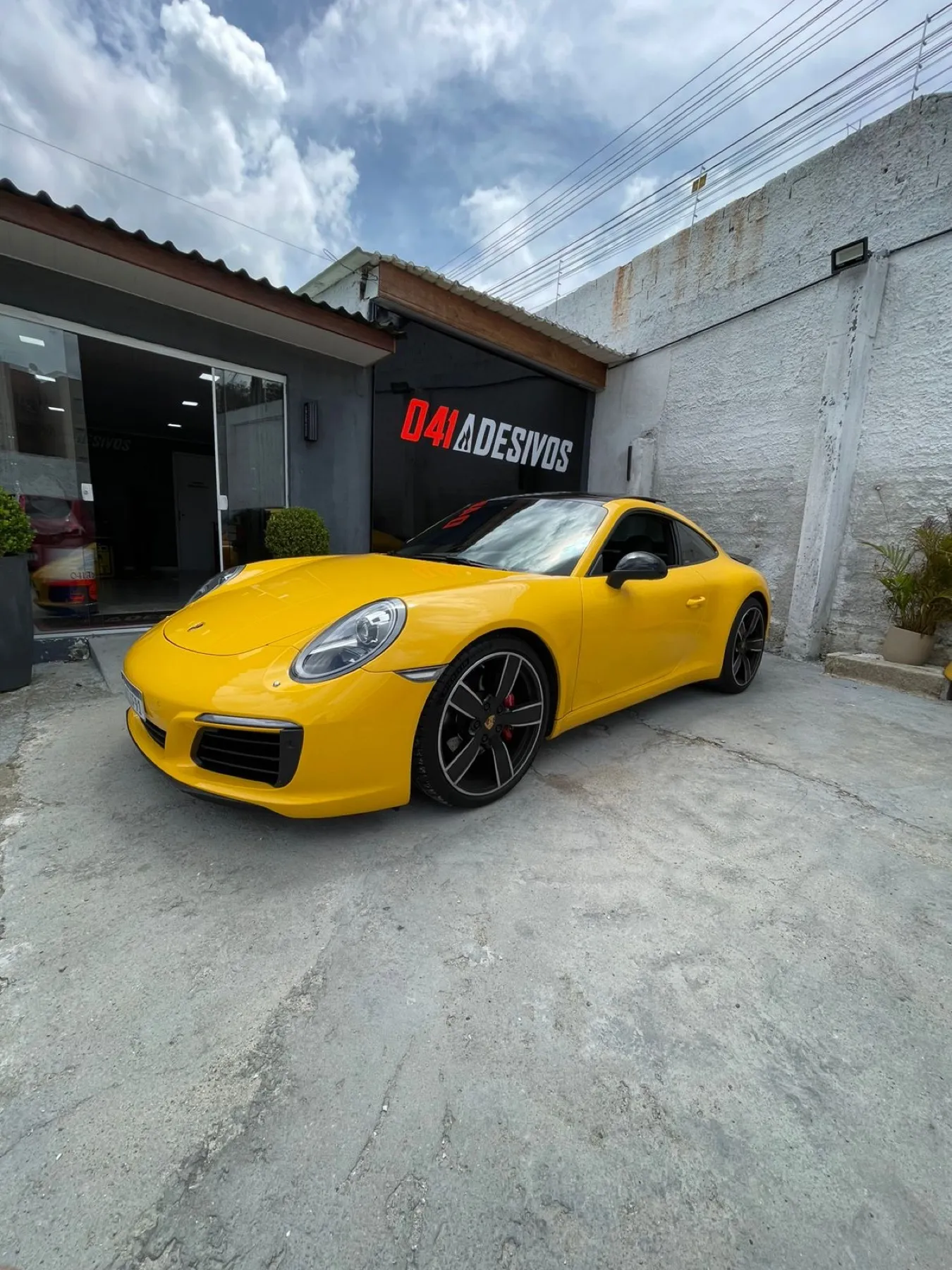 Porsche 911 amarelo em frente à fachada da 041 Adesivos